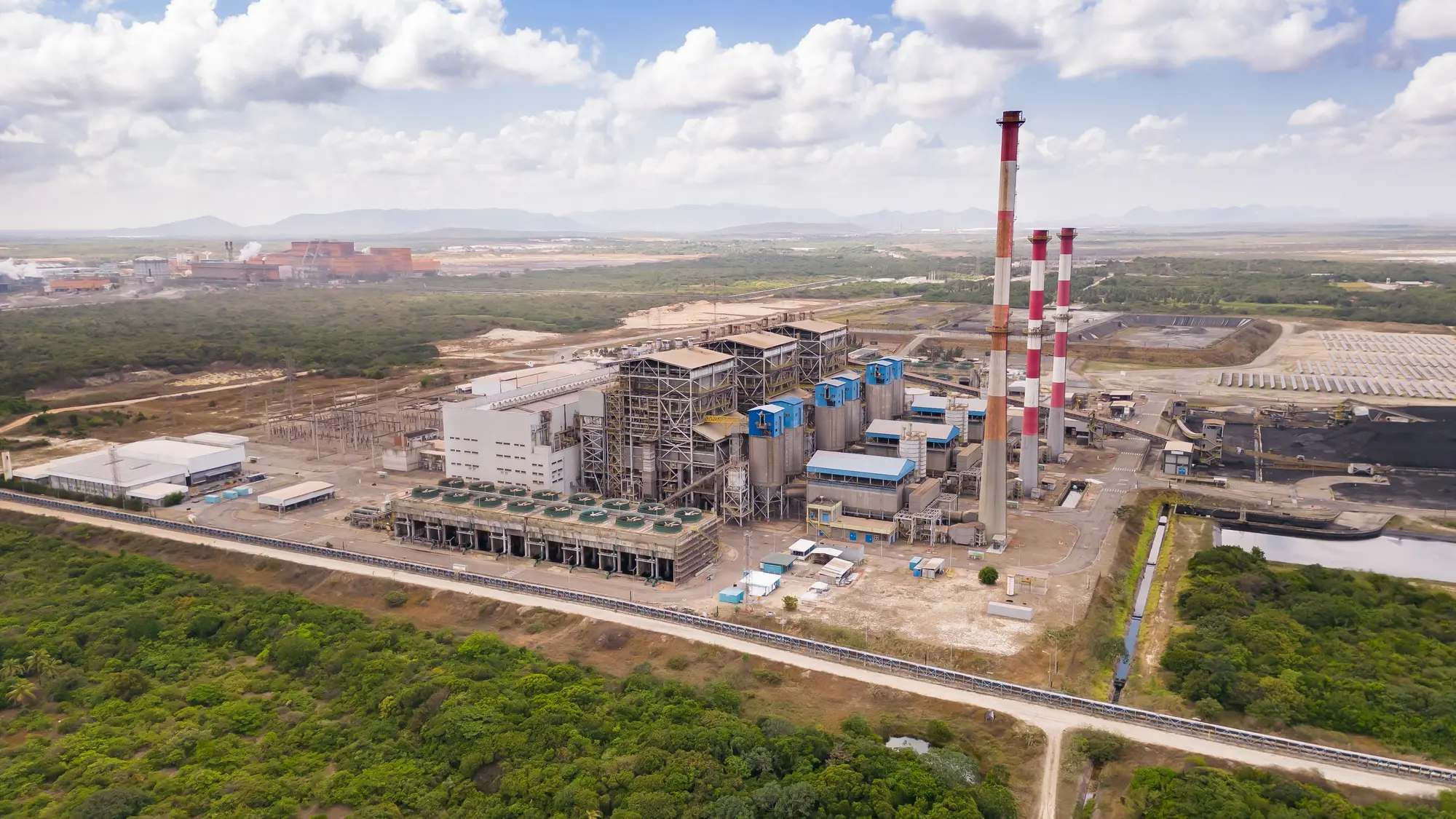 Vista aérea de usina termelétrica no Ceará, com chaminés listradas e a serra ao fundo