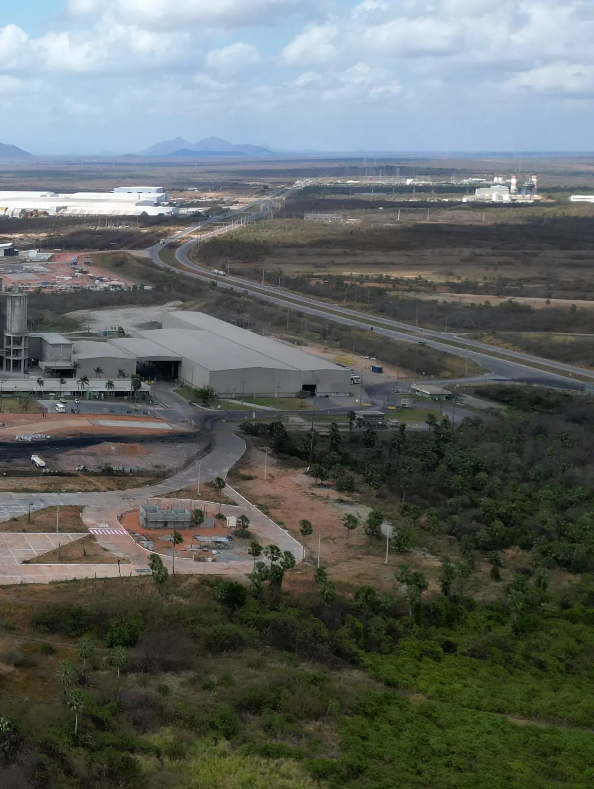 Fábrica de cimento com silos e a serra ao fundo, vista de drone