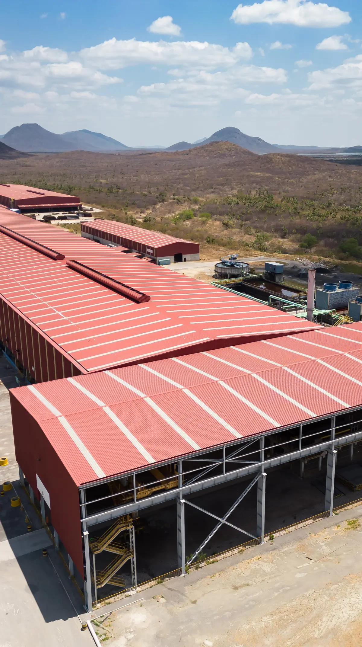 Galpão de cobertura vermelha de siderúrgica com a serra ao fundo