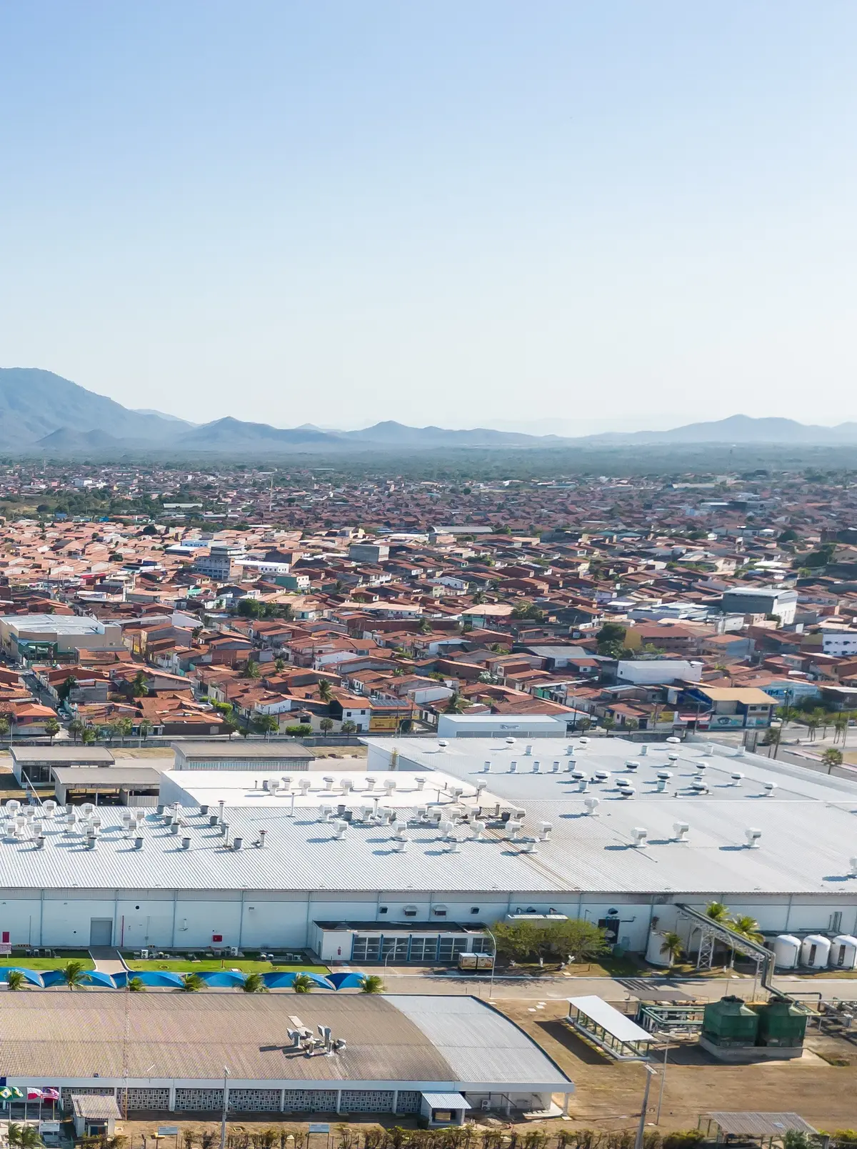 Fábrica em área urbana com a serra ao fundo, vista de drone