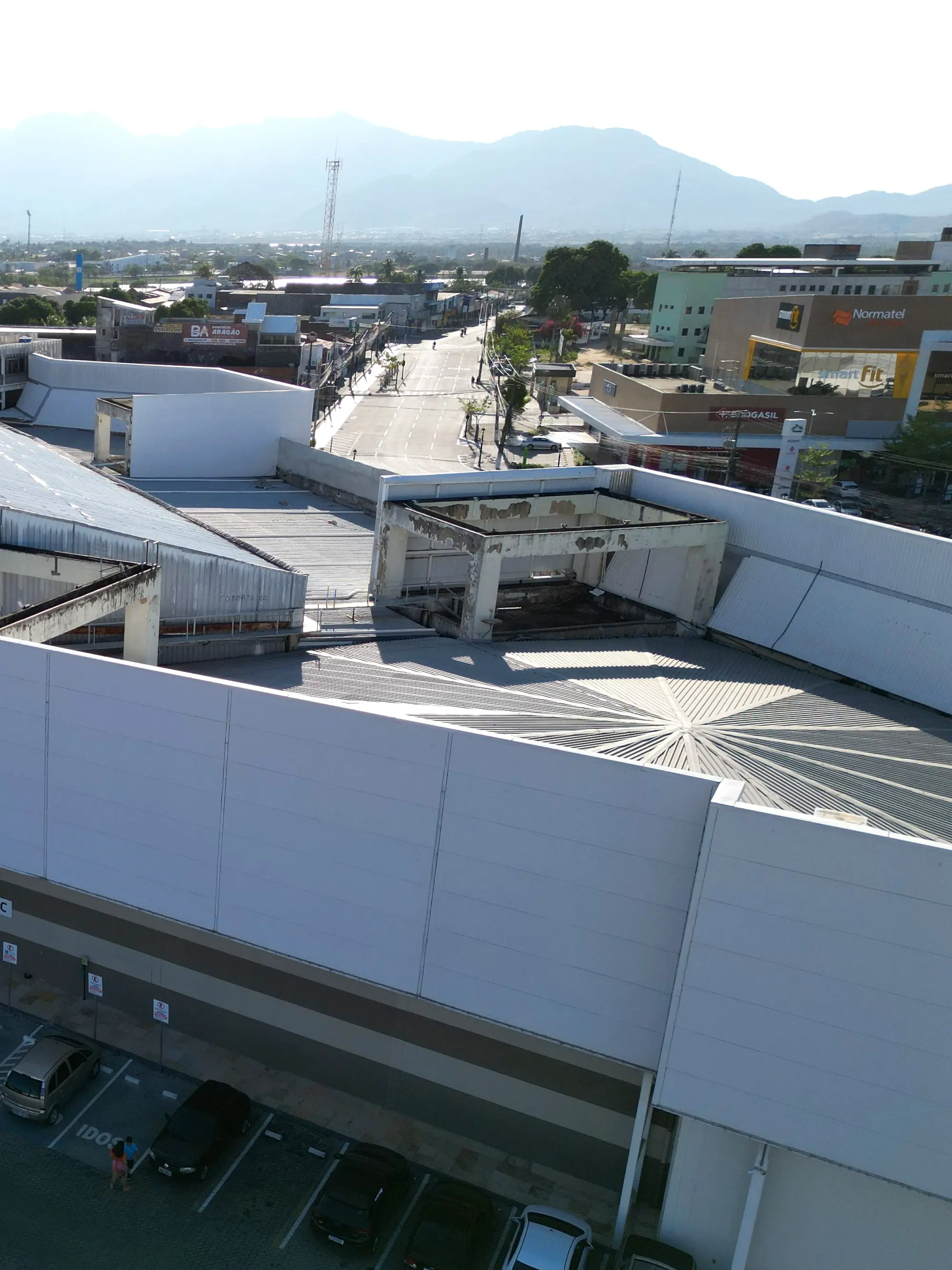 Shopping center e estacionamento vistos do alto, com a serra ao fundo